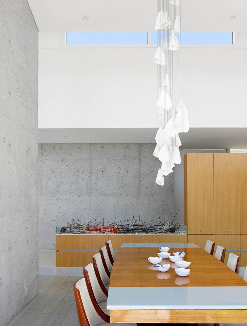 Divided by a concrete wall, the next section is the dining room, that has a sculptural pendant light hanging above the table. Cabinetry adds extra storage space to the area.