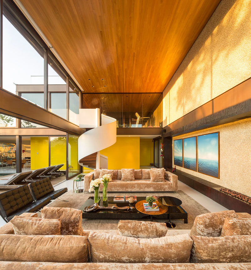 This large living area has a double-height ceiling, a bright yellow feature wall and a wooden ceiling.