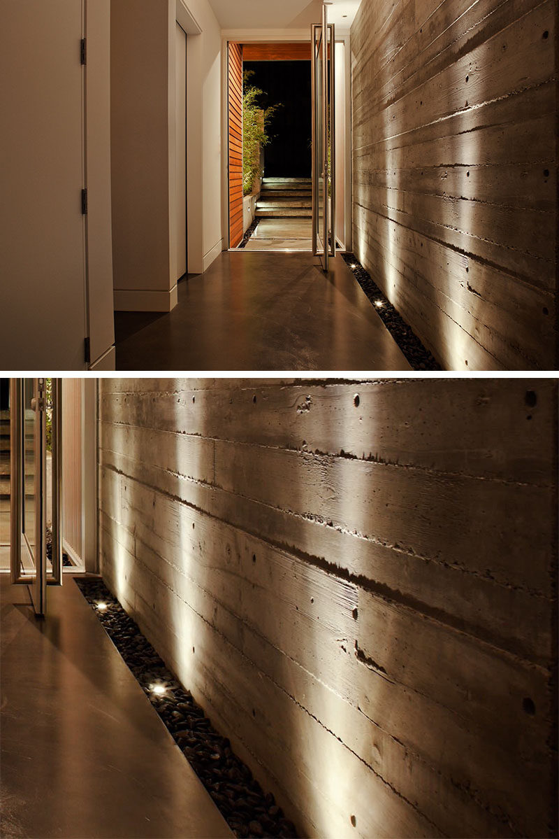 7 Interiors That Use Dramatic Uplighting To Brighten A Space // The strip of pebbles and lights that run along the side of the wall of the entry way in this house, uniquely welcomes people into the home and helps the texture of the concrete wall stand out.