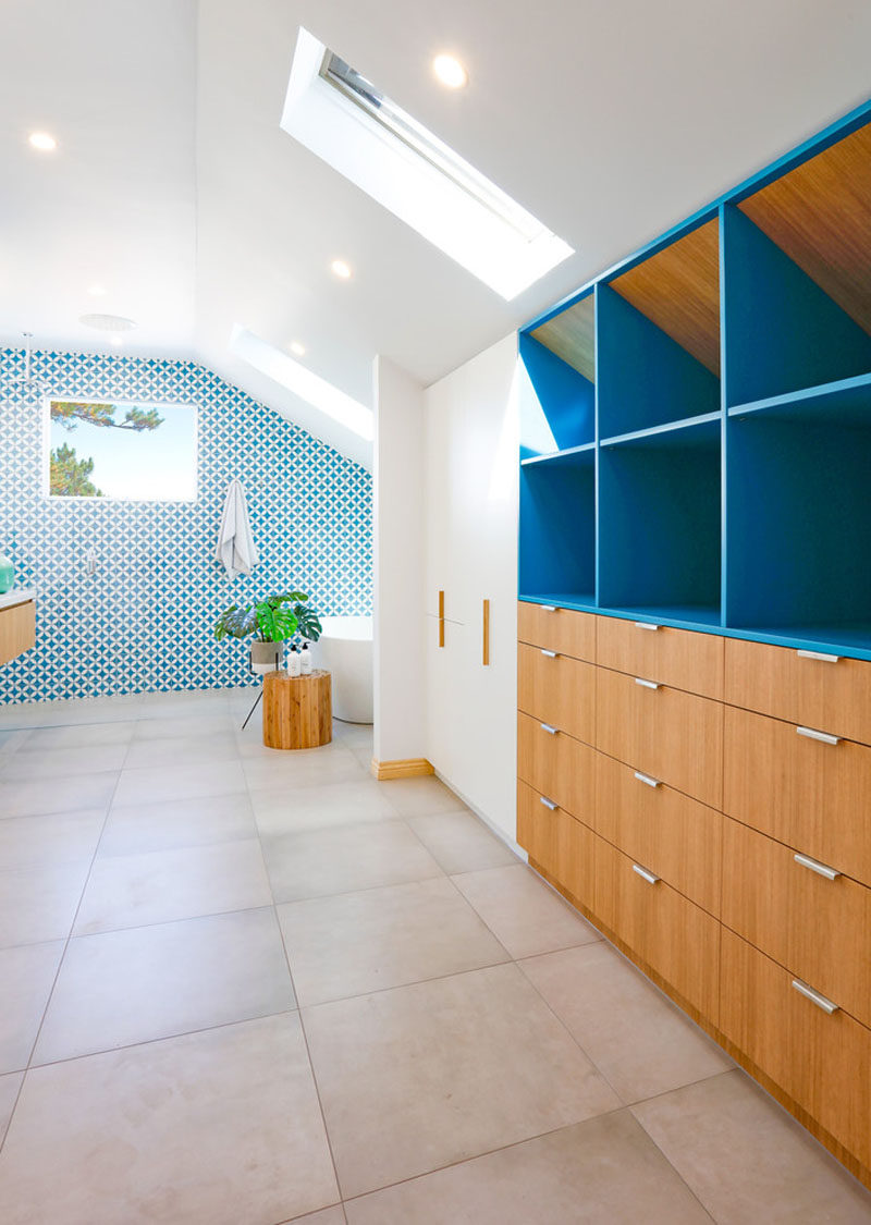 The most attention grabbing aspect of this mostly-white modern bathroom is the bright blue and white patterned tile accent wall that works well with the large grey porcelain floor and the floating wood vanity and built-in closet.
