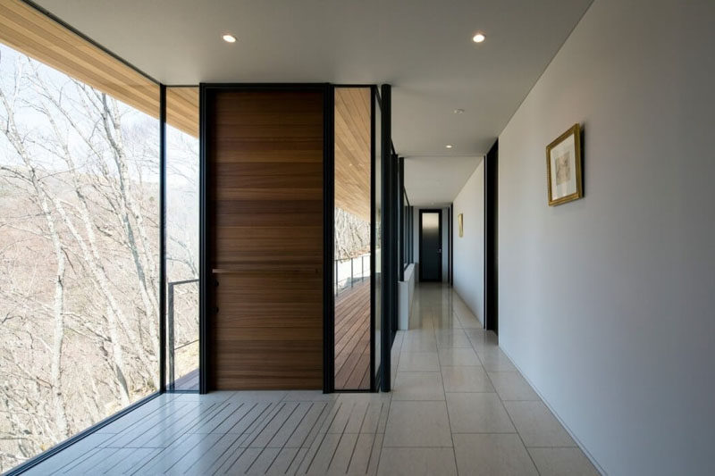 This modern front door with a horizontal wood pattern is surrounded by windows that look out at the trees surrounding the home.
