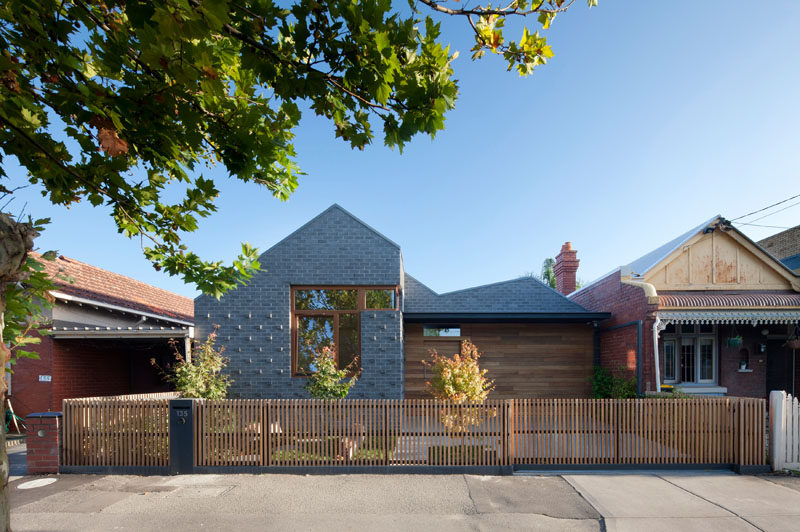 At the front of this modern house, a combination of grey brick and wood paneling covers the front exterior. Protruding bricks at the front add texture and depth, while the wood paneling that matches the trims of the windows and the fence adds warmth and a natural look to the home.