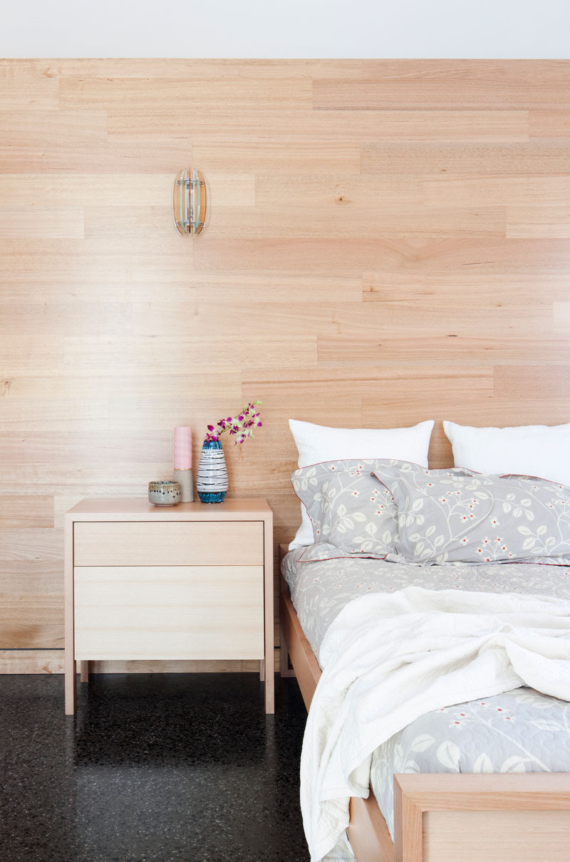 In this modern bedroom, light wood paneling lines the wall behind the bed and matches the bed frame and the night stand, creating a unified look, adding warmth, and keeping the room bright.