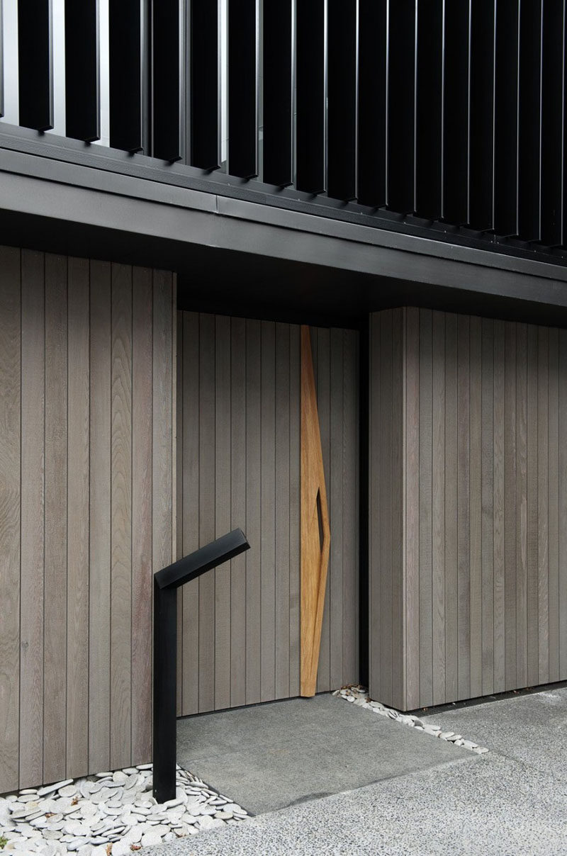 The vertical grey wood panels of this wood front door are interrupted by a sculptural door handle that runs the length of the door.