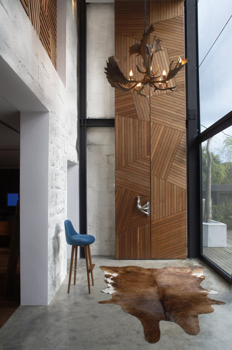 Light wood strips arranged in a geometric fashion make up these 23 foot tall doors that lead into the study of the home, while sculptural metal door handles help you pry the doors open.