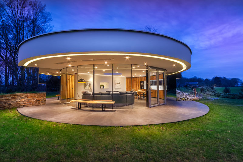 Located in an opening in a Dutch forest, this small, circular modern house was designed for a couple and their dogs. The circular house features curved windows that wrap around the front of the home and mirrors at each end give the appearance that the windows never end.