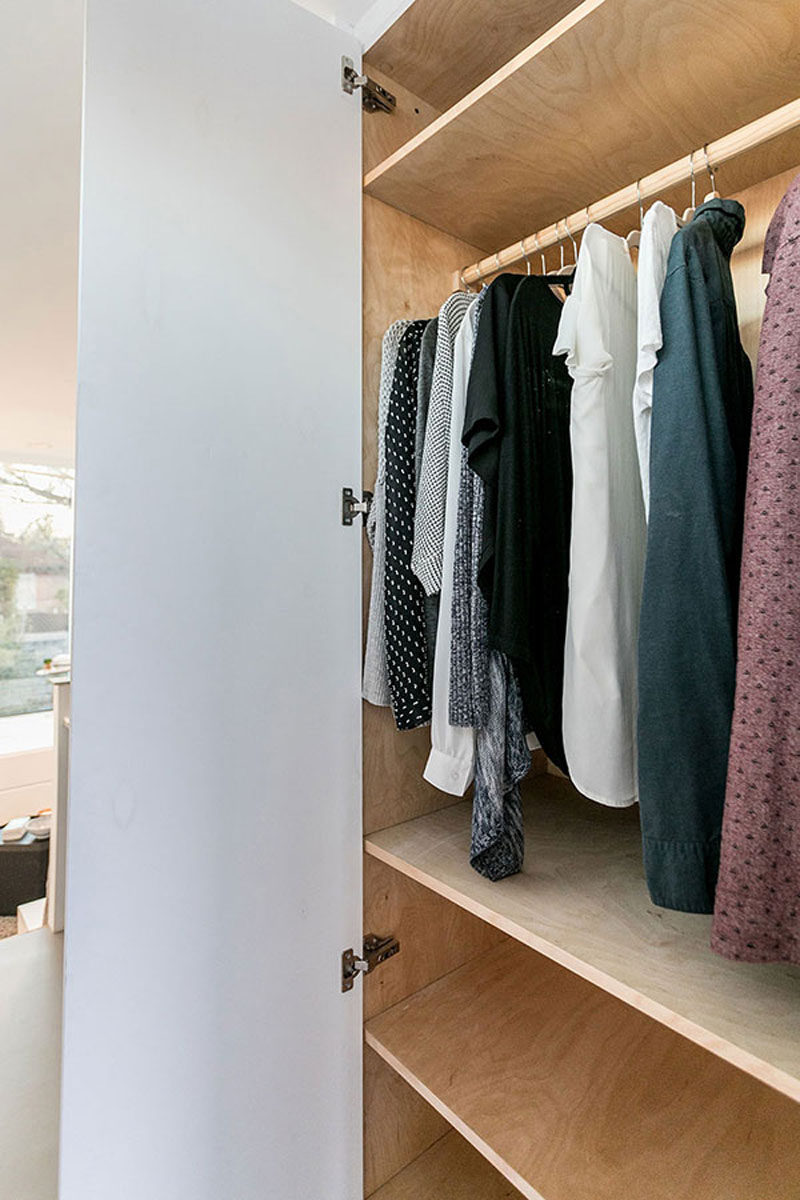 In this modern tiny house, there's a storage closet that has a bar for hanging clothes and plenty of wood shelves.