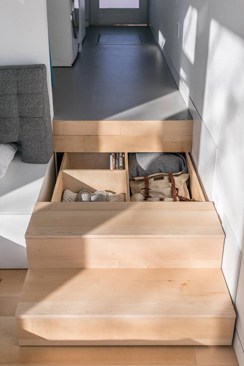 In this modern tiny house, the wooden stairs that lead down to the living room have hidden pull-out storage drawers.