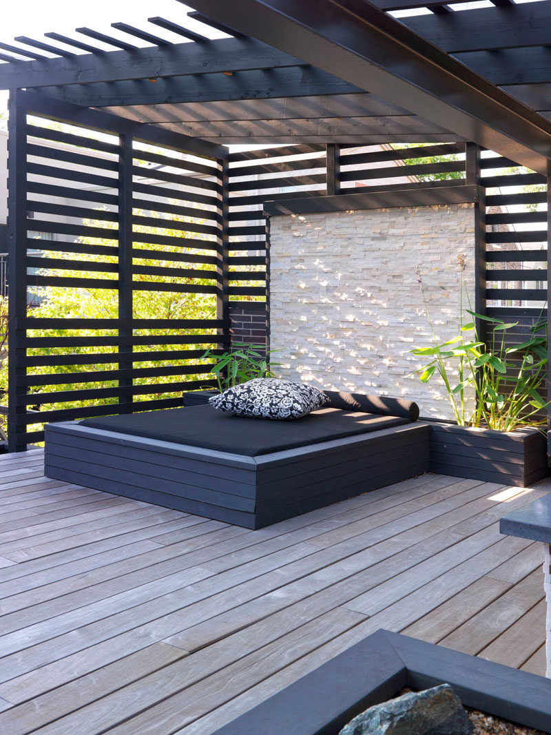  This built-in outdoor day bed with a stone wall and planters sits underneath a pergola that provides shade.