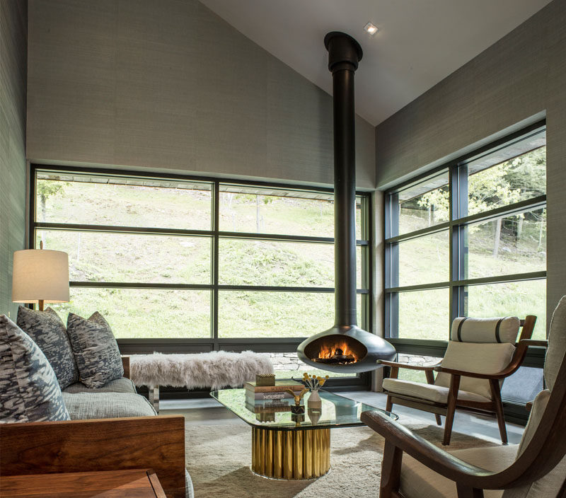 This modern living room has plenty of windows for natural light and views of the landscape outside, as well as a hanging fireplace for when it gets cold.