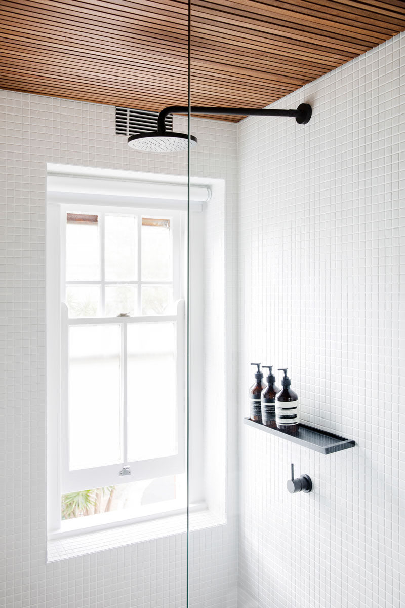 Белые плитки и деревянные элементы имеют в этой современной ванной комнате, а выпадающий слепой обеспечивает секретность без блокировки слишком много света из окна.