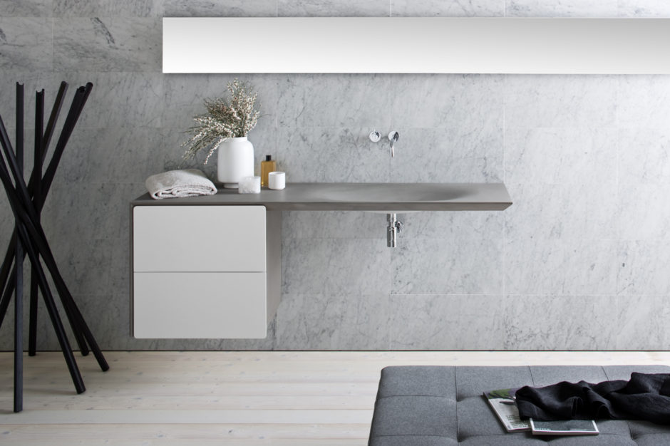 This modern, seamless grey stone sink is wall mounted with two white drawers and a chrome faucet. 