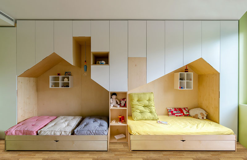 This fun and modern kid's bedroom has a custom wall unit that features plenty of storage and two beds in mini houses.