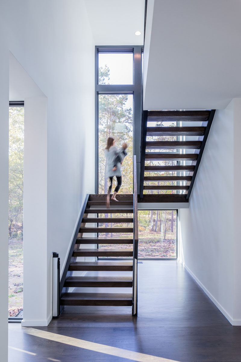 Темные деревянные лестницы сильно контрастируют с белыми стенами в этом современном доме и ведут на верхний этаж дома.  Окна охватывают высоту лестницы и позволяют обилие естественного света.