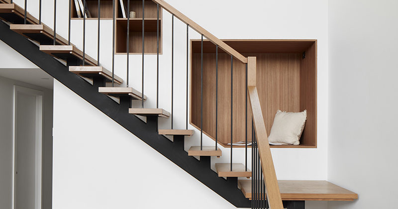 This modern wood and steel staircase features a wood-lined seating nook and bookshelves that have been built into the wall.