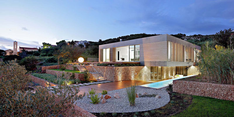 Architecture firm LOG-URBIS have designed a modern house on a sloped site on the island of Pag in Croatia, that has a terraced landscaped yard, a long swimming pool and water views. #ModernArchitecture #ModernHouse #LandscapedYard #SwimmingPool
