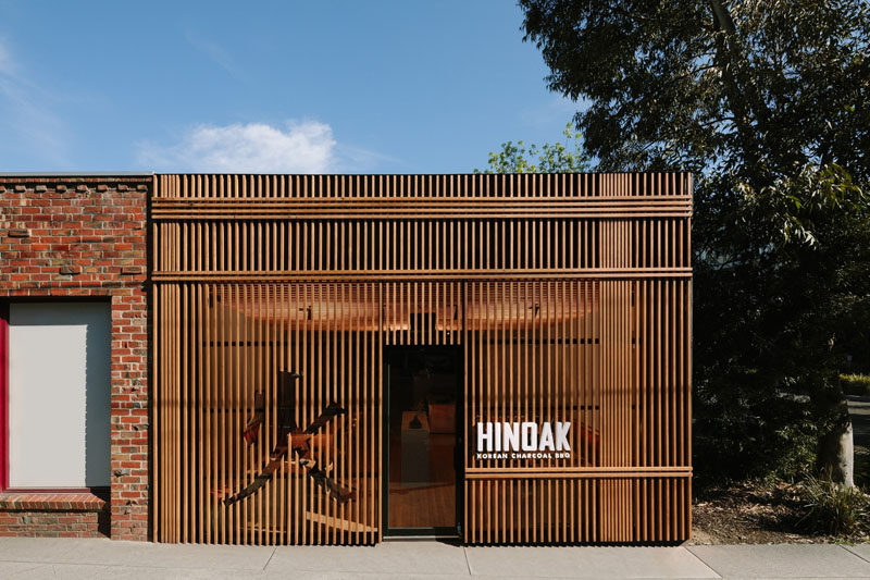 Inspired by traditional Chinese iconography and the work of Japanese architect Kengo Kuma, the facade of this modern Korean BBQ restaurant has a slatted wood exterior with a character cut-out and bright white signage. #WoodFacade #RestaurantDesign
