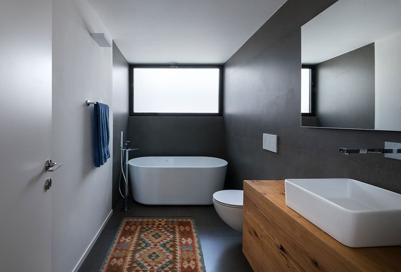 In this bathroom, grey walls and floors have been combined with a white freestanding bathtub and a large wood vanity to create a modern look. #ModernBathroom #BathroomDesign