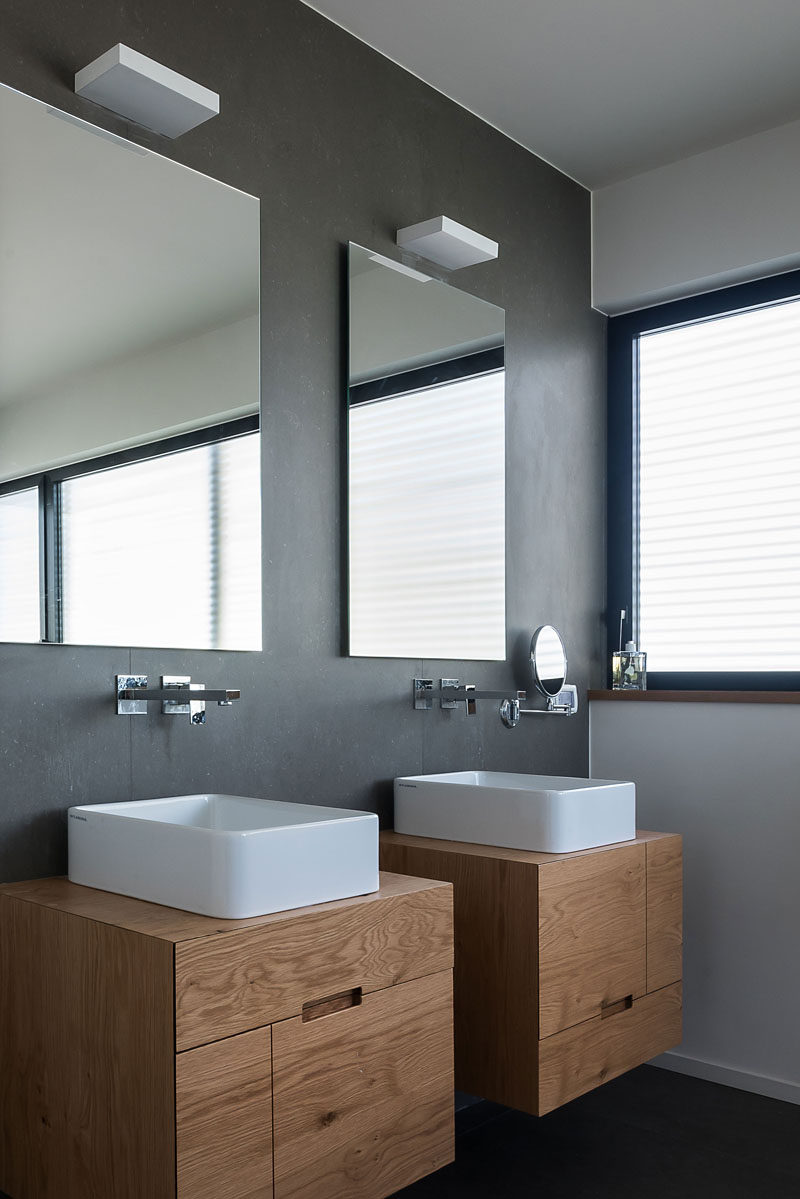 In this bathroom, grey walls and floors have been combined with a white sinks and two wall-mounted wood vanities to create a modern look. #ModernBathroom #ModernWoodVanity