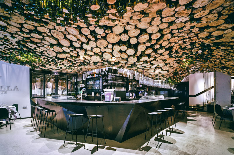 A Wavy Installation Of Cut Logs And Green Glass Cover The Ceiling