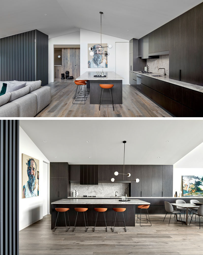 The entryway of this modern house opens up to a large great room, with the kitchen and dining room along one side, and the living room on the other. Dark wood cabinets have been paired with light countertops in the kitchen. #ModernKitchen #KitchenDesign #DarkWoodKitchen