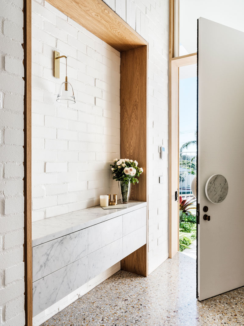 Inside the front door of this modern house, there's a built-in wood framed sideboard in the entryway, while a white brick wall adds texture to the space. #Entryway #ModernInteriorDesign