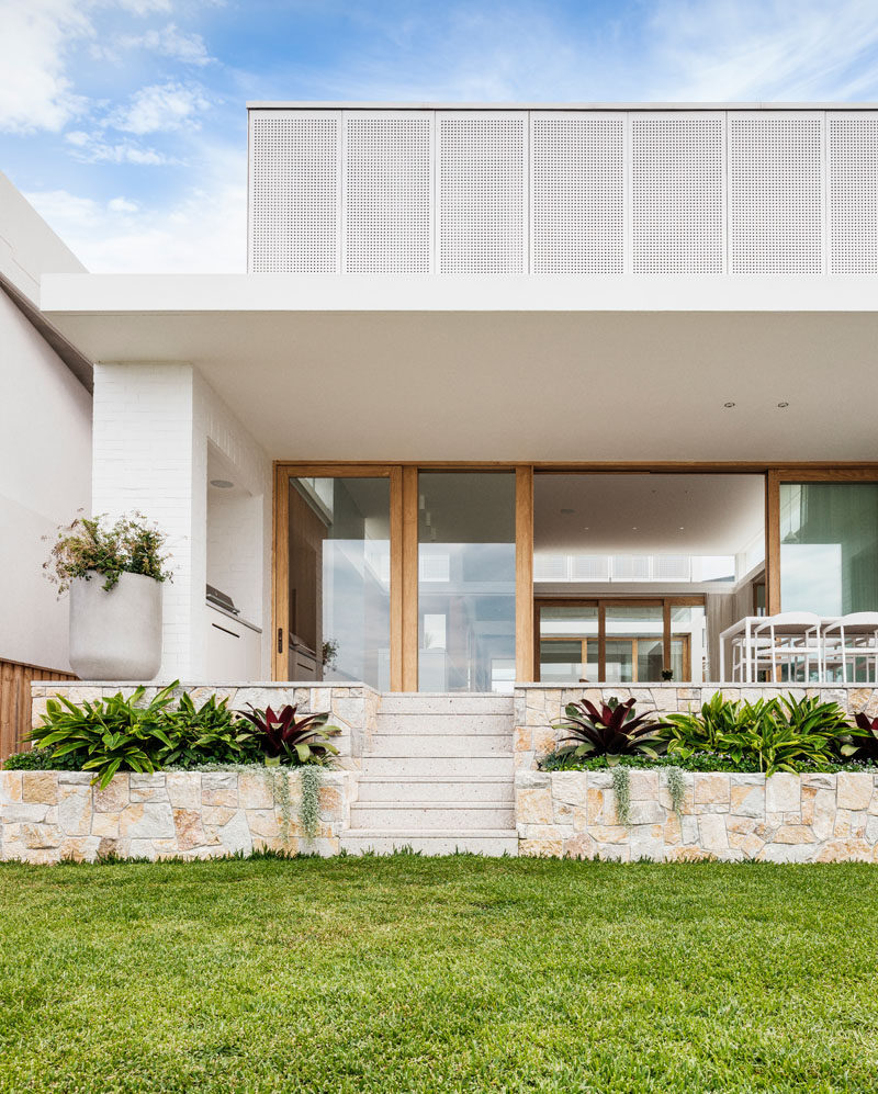 As this modern house is on a sloped site, sandstone planters on either side of the stairs have been included in the landscape design, separating the outdoor dining area and the grassy area below. #Landscaping #Sandstone #ModernHouse