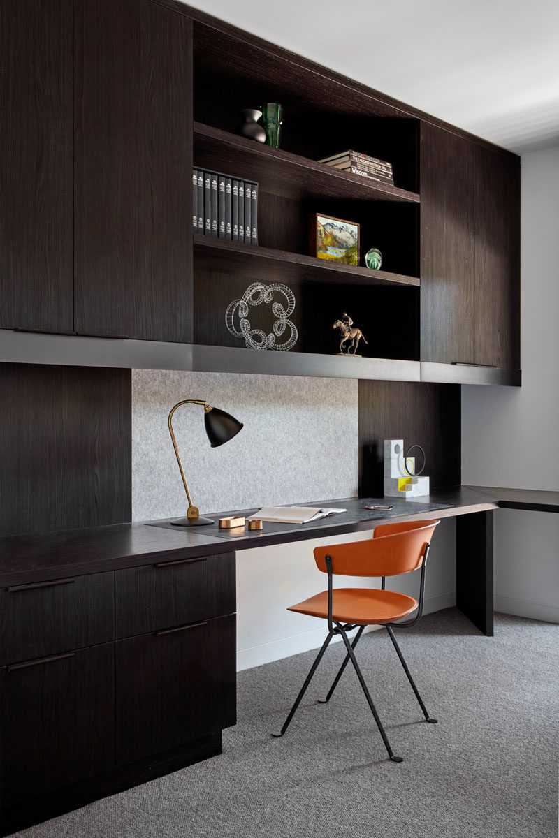 In this modern home office, dark cabinets with open shelving contrast the white walls, while the orange and black chair adds a pop of color. #HomeOffice #ModernHomeOffice #DarkCabinetry