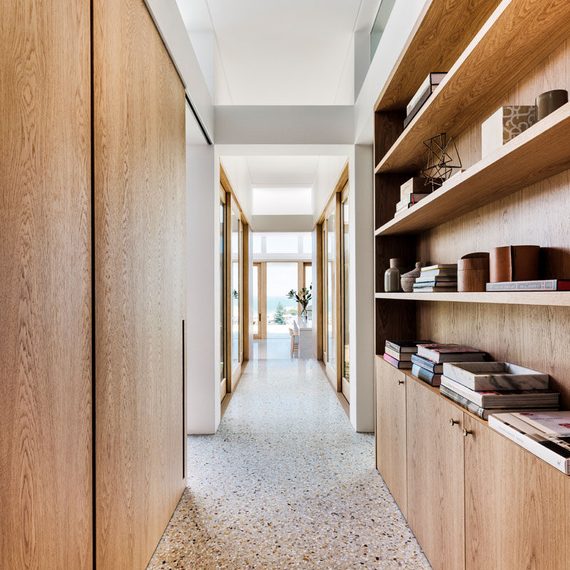 This modern house has a hallway with wood elements, like a bookshelf and door frames, that leads from the front of the house to the living area and kitchen. #ModernHallway #WoodShelving