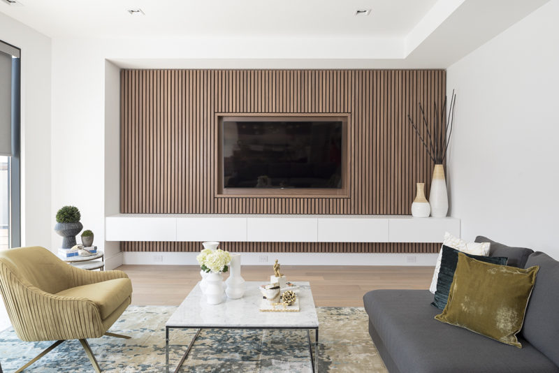 This modern living room features a wood slat accent wall that surrounds the TV and provides a row of white storage cabinets. #TVWall #InteriorDesign #AccentWall #LivingRoom