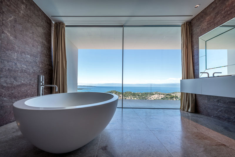 Large floor-to-ceiling windows provide this modern bathroom with a view of the water. #Bathroom #ModernBathroom #Windows