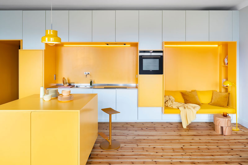 This renovated 1920s apartment in Stockholm received a modern makeover, with a custom designed wall that includes yellow built-in sections that house a kitchen and a seating nook. #InteriorDesign #Kitchen #SeatingNook