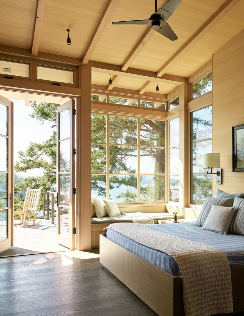 This contemporary master bedroom has a built-in window seat, a high sloped ceiling, and access to a deck. #BedroomDesign #WindowSeat