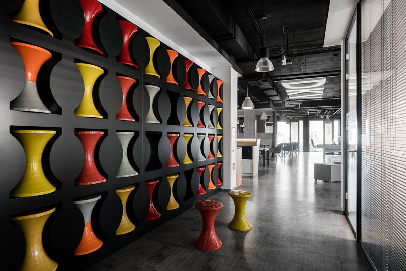 This modern office has a wall with cut-outs, that's dedicated to the storage of hourglass stools. When the stools aren't in use, they are placed into the empty spots in the wall, creating more room for walking around. #Stools #OfficeDesign #Workplace #WallStorage