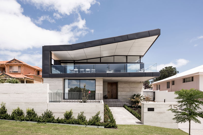 The roof, along with an angular plan, allows this modern house to take advantage of the views of the surrounding area, while black zinc has been used on the upper half of the house to create contrast with the light colored exterior walls. #ModernHouse #ModernArchitecture #HouseDesign #CurbAppeal
