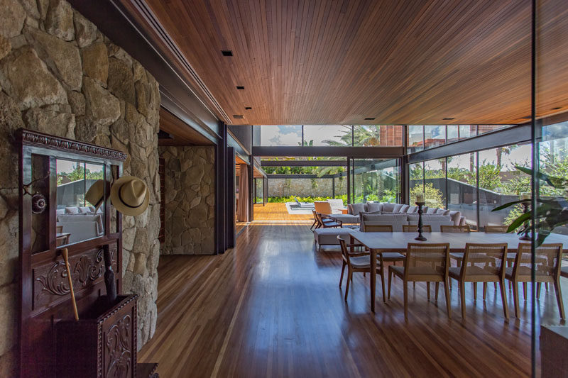 The social areas of this modern house are located on the main floor of the home. Large aluminum and glass frames help to bring the landscaping into the interior environments, making them appear larger. #ModernHouse #StoneWall #InteriorDesign