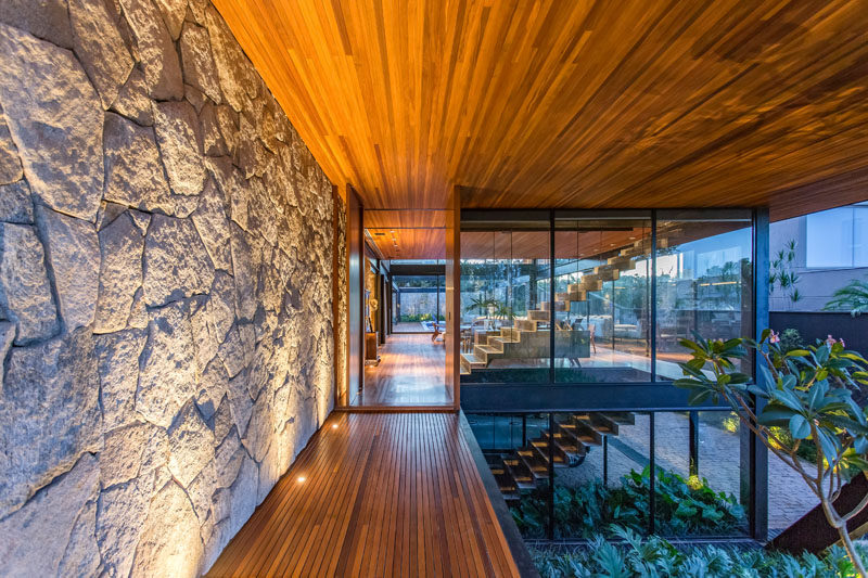Wood veneers, natural stones, and metal sheets were incorporated into the design of this modern house, helping to define the volumes and making the interior spaces more welcoming. #ModernHouse #StoneWall #WoodCeiling #ModernArchitecture