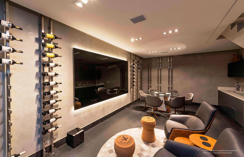In this modern basement, there's a bar and lounge with a large television on the wall, and floor to ceiling wine racks to display the home owner's wine collection. #Basement #WineRack