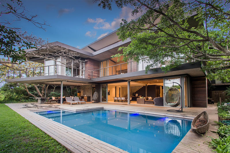 Large sliding glass doors open the main floor of this modern house to the yard, swimming pool and its surrounding deck. #SwimmingPool #ModernHouse #Deck #OutdoorLivingRoom