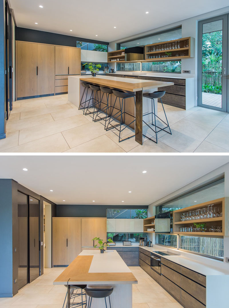 In this modern kitchen, the centrally located island has been designed to accommodate seating, white open shelving along one wall shows off the glassware collection. #ModernKitchen #KitchenDesign #KitchenIdeals