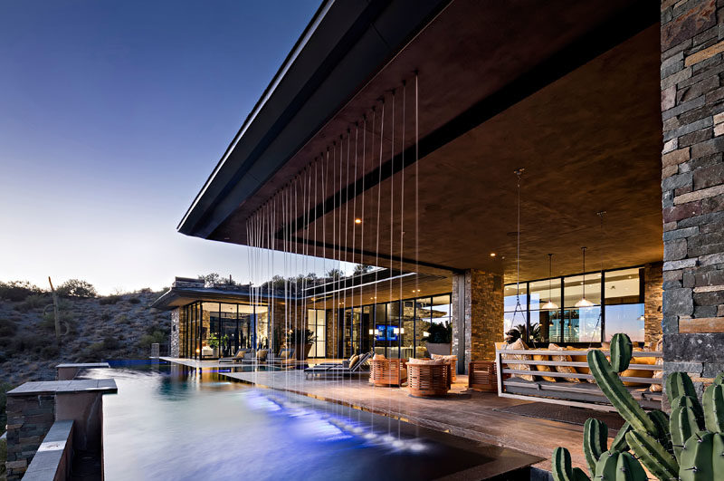 This modern house has a rainfall water feature that connects with the pool, and is located beside the outdoor living room, that also has a bbq and dining area. #SwimmingPool #Flooring #Architecture #OutdoorLivingRoom #Fireplace #WaterFeature