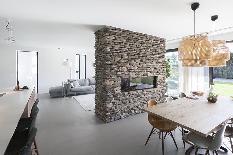 Apart from separating the dining area and living room, this stone accent partition is home to a linear fireplace on the dining room side, and on the opposite side, a built-in television with storage below. #StonePartition #StoneFireplaceSurround #StoneWall