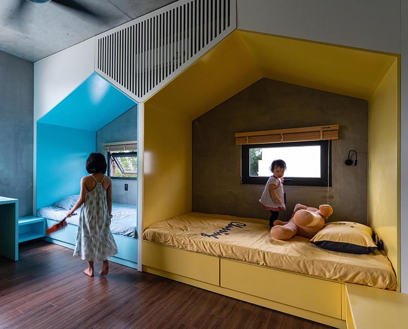 This modern bedroom, which features wood floors, has two mini 'houses' that define the separate sleeping areas for the children. The houses, each with their own window, create a little nook for each child, giving them their own space when needed, while a combined shelf and desk is color matched to the bed. #KidsBedroom #BedroomDesign #SharedKidsBedroom #ChildrensBedroom #ModernKidsBedroom