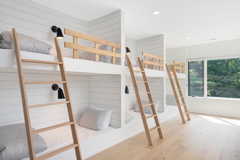 In this modern bedroom, three sets of built-in bunk beds with wood ladders and safety rails, create a place for six people to sleep. Each bunk has a niche, outlets and an individual switch for their separate light. #Bedroom #BunkBeds #MultipleBunkBeds #ModernBedroom