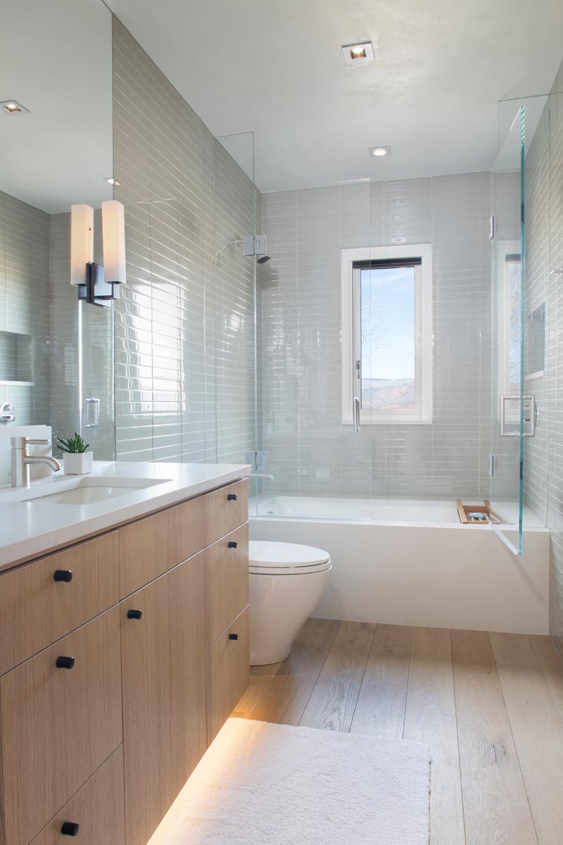 In this modern bathroom, light grey tiles cover the wall, while a wood vanity has hidden lighting beneath it to create a soft glow. #ModernBathroom #BathroomDesign #GreyTiles