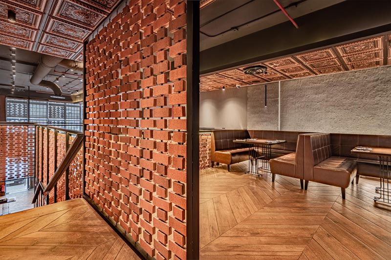 Open brick walls wrap around the different areas of this restaurant, like above the kitchen and along the stairs. They provide visiual interest and a sense of privacy on the upper level of the interior, without blocking the light. #RestaurantDesign #BrickWalls #ScreenIdea #BrickScreen