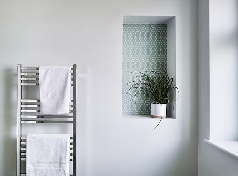 This modern bathroom features a recessed shelf, which is large enough to display a plant, and includes small hexagon penny tiles with white grout. It also helps to add a pop of color to the plain grey wall, and draws attention away from the toilet below. #BathroomShelf #BathroomIdeas #RecessedShelf #PennyTile #BathroomDesign