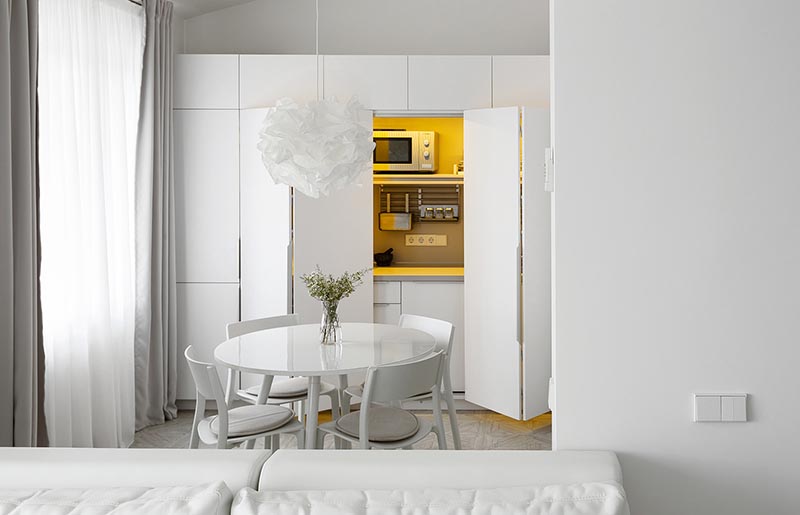 This modern and minimalist white apartment has the kitchen hidden within a closet in the dining area. #MinimalistKitchen #HiddenKitchen #KitchenDesign
