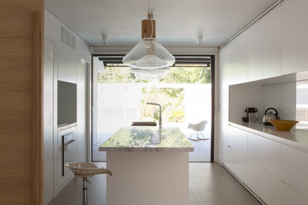 This smaller white kitchen has a central long island with pendant lights hanging above.