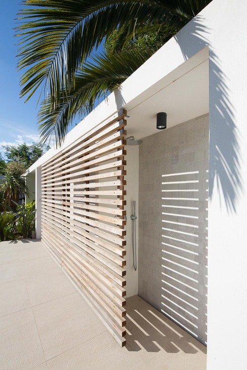 This outdoor shower is hidden behind a wooden slat wall.